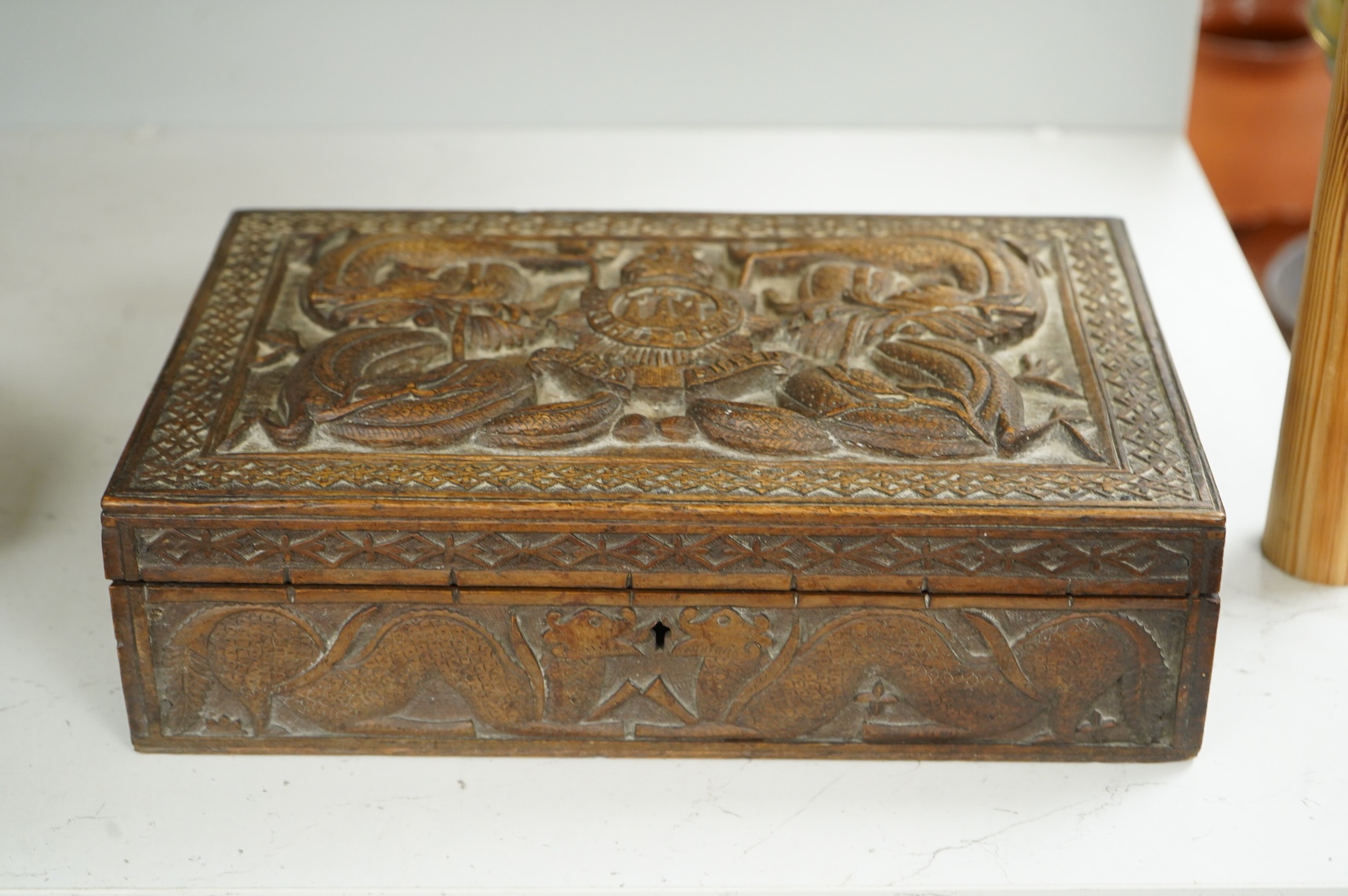 A Burmese military themed carved box, early 20th century, heavily carved with the insignia of the Devonshire Regiment to the lid, surrounded by mythical dolphins, serpents, and geometric patterns, with segmented interior